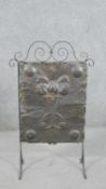 An Arts & Crafts wrought iron fire screen, with a planished copper panel, depicting flowers,