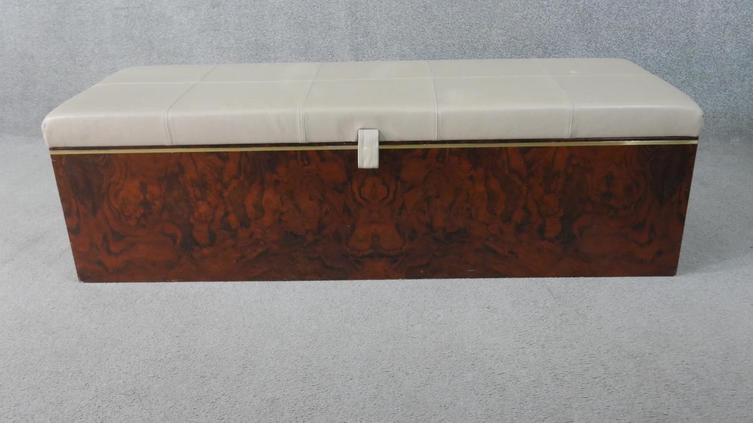 A figured walnut Ottoman, of slender rectangular form, with a white upholstered leather cushion lid,