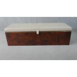 A figured walnut Ottoman, of slender rectangular form, with a white upholstered leather cushion lid,