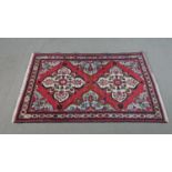 A handmade Persian Hamadan rug with repeating floral motifs across the madder ground within