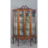 An Edwardian mahogany display cabinet, with a swan neck pediment, over a pair of bevelled glass