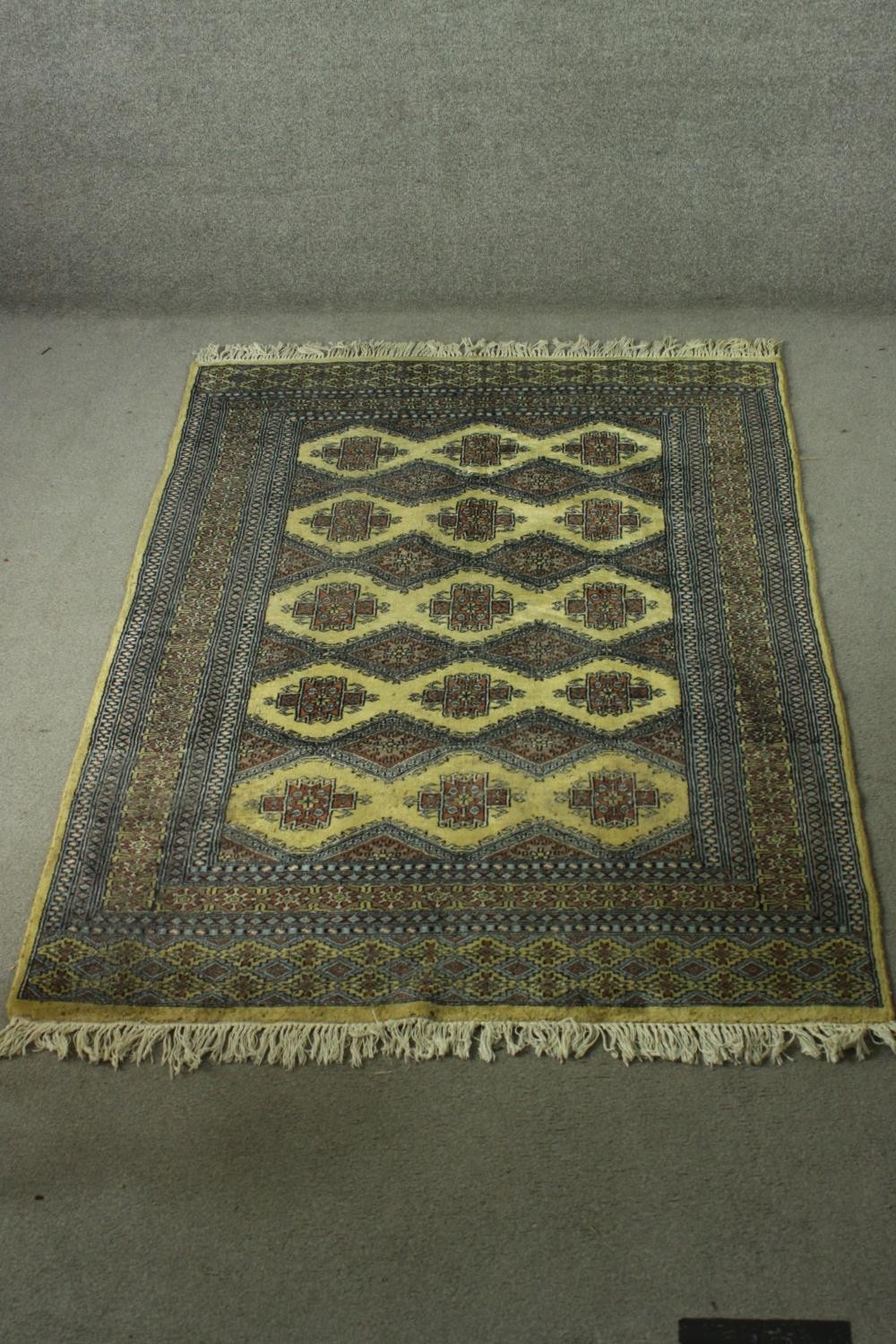 A Pakistan Bokhara rug with repeating stylised foliate motifs on a biscuit ground within multiple