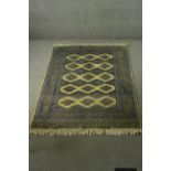 A Pakistan Bokhara rug with repeating stylised foliate motifs on a biscuit ground within multiple