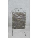 An Arts & Crafts wrought iron fire screen, with a planished copper panel, depicting flowers,