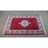 A hand made Moroccan rug with central floral medallion on a burgundy ground within a foliate border.