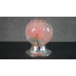 A glass liquid filled globe containing a large plastic allium flowerhead on metallic effect base.