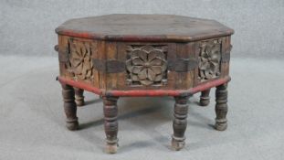 An Indian hardwood octagonal low table, the sides formed of carved panels, with one cupboard door
