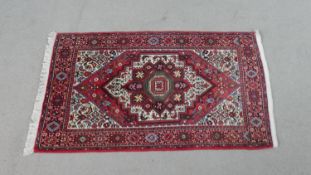 A Persian hand made Senneh rug with triple medallion on burgundy ground within spandrels and