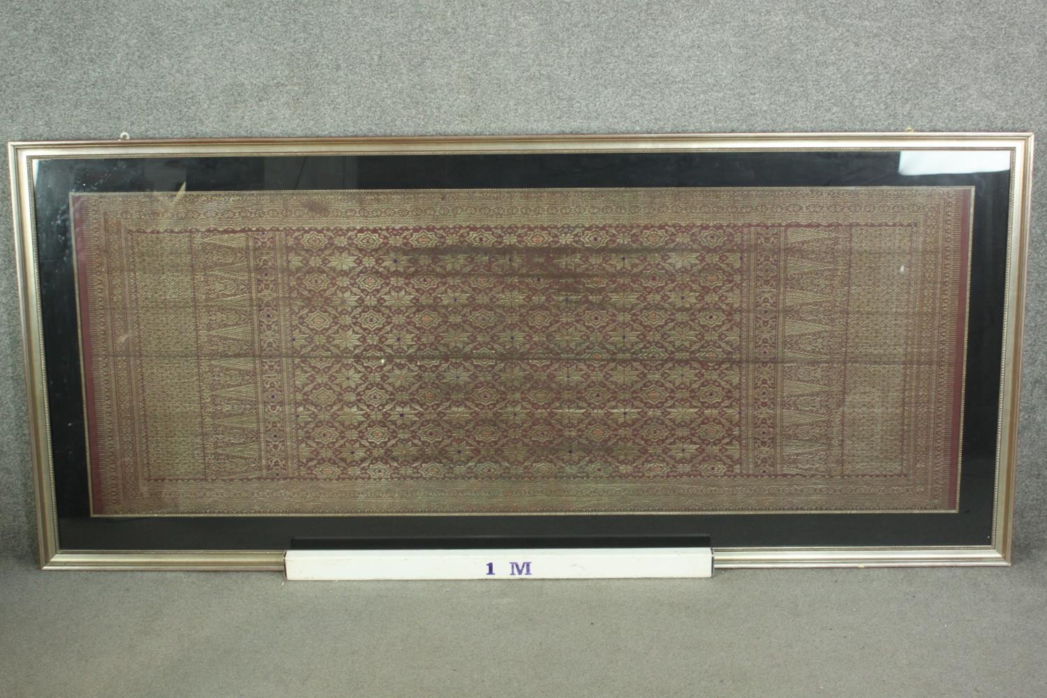 A framed and glazed Indonesian plum ground and gold thread woven silk work. H.102 W.229cm. - Image 2 of 5