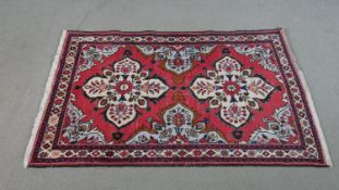 A handmade Persian Hamadan rug with repeating floral motifs across the madder ground within