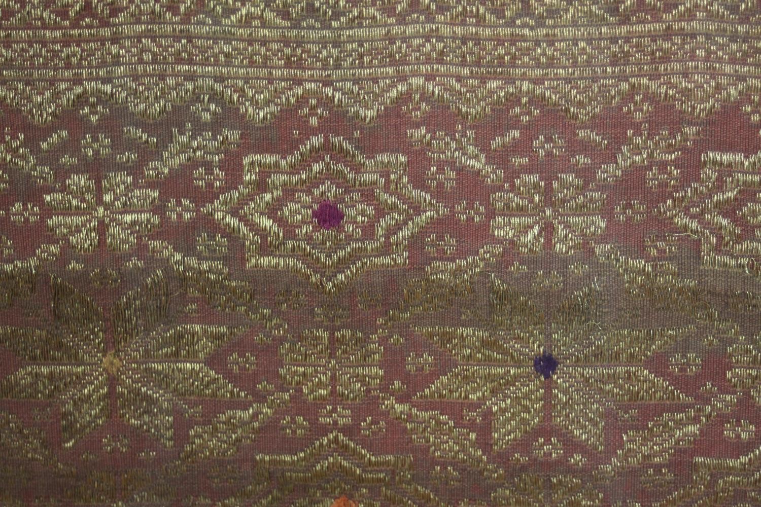 A framed and glazed Indonesian plum ground and gold thread woven silk work. H.102 W.229cm. - Image 5 of 5