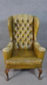 A wing back armchair, upholstered in green leather, with a button back, on cabriole legs, joined