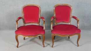 A pair of French walnut Louis XV style fauteuil armchairs, upholstered in red fabric to the back,