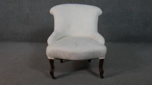 A Victorian nursing chair, upholstered in ivory fabric, with a scrolling buttoned back, on scrolling