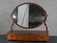 A George III mahogany toilet mirror, the oval mirror in a swing frame, over a bow fronted base of