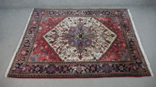 A hand made Persian Heriz carpet with central lozenge medallion on a burgundy field. H.196 W.152cm