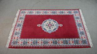 A hand made Moroccan rug with central floral medallion on a burgundy ground within a foliate border.