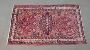 A Persian Hamadan rug with triple hooked medallions on a pale burgundy ground within foliate