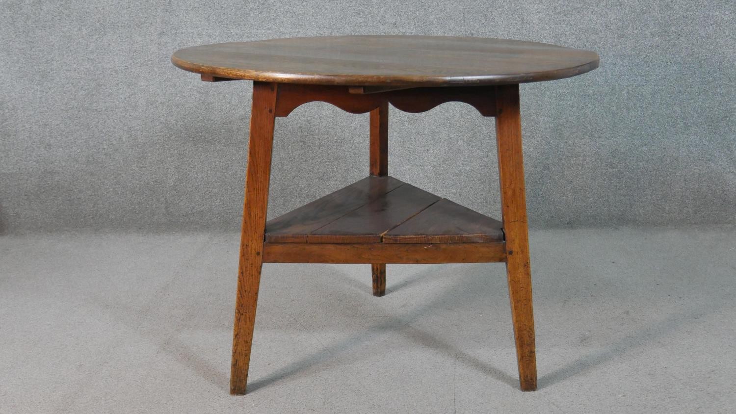 A 19th century country oak cricket table with shaped frieze on splay supports united by an