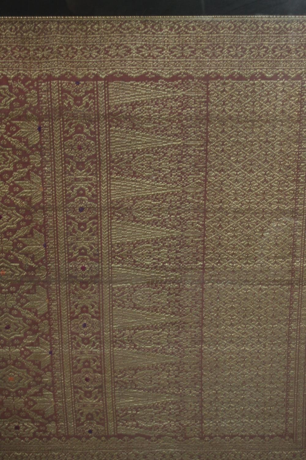 A framed and glazed Indonesian plum ground and gold thread woven silk work. H.102 W.229cm. - Image 4 of 5