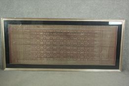 A framed and glazed Indonesian plum ground and gold thread woven silk work. H.102 W.229cm.
