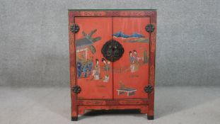 A 20th century Chinese red lacquered cabinet, painted with ladies in a garden, with two doors, on