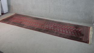 A Pakistan Bokhara runner with repeating gul motifs on a burgundy ground within flowerhead