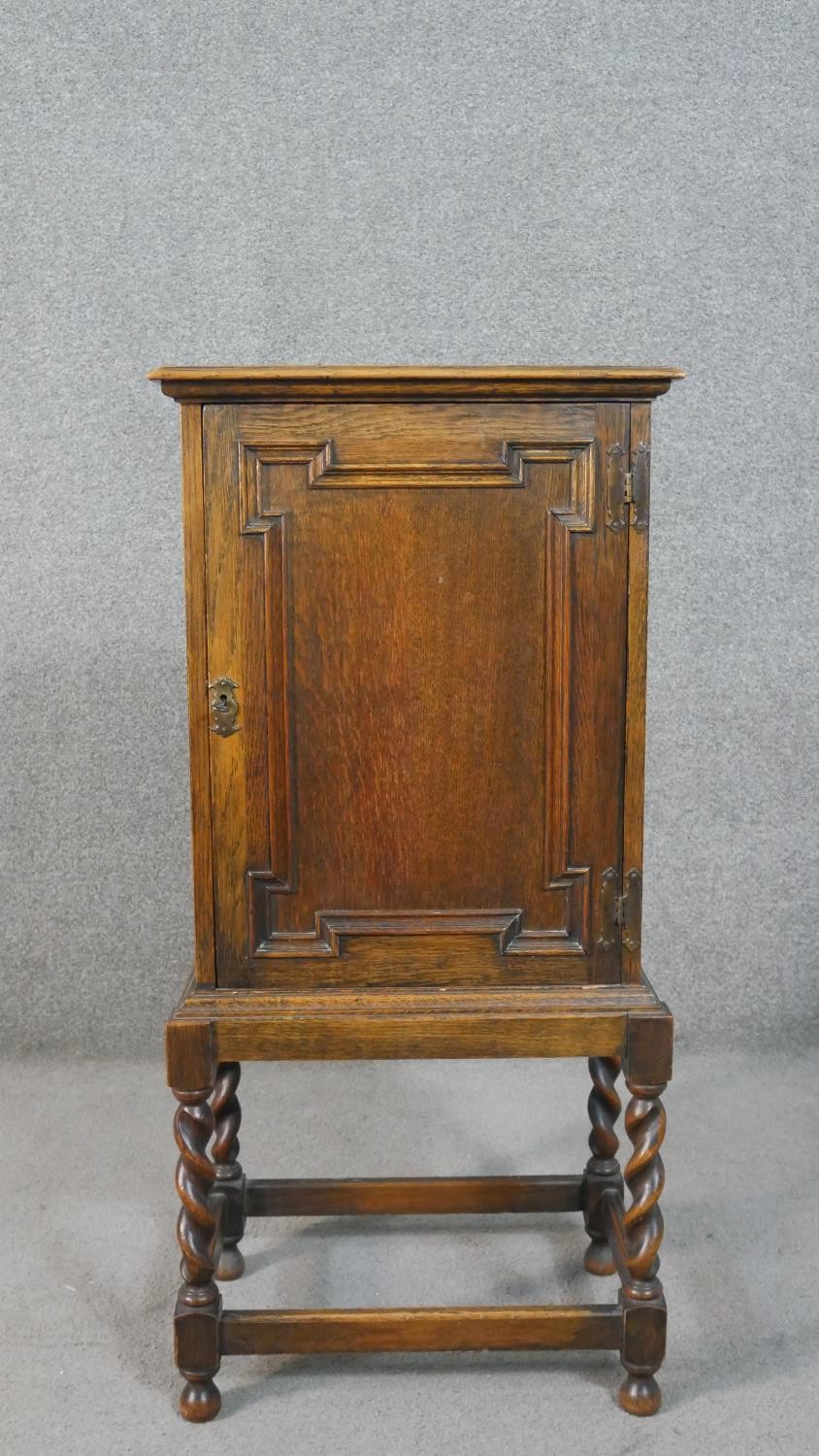 A Jacobean style oak cabinet with lozenge panel door enclosing a fitted interior on a barleytwist
