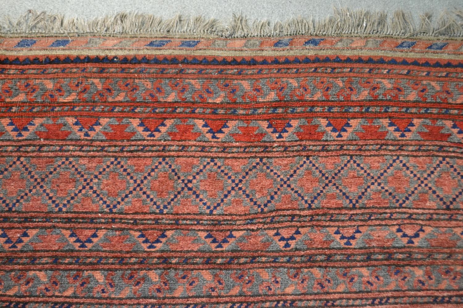 A handmade Afghan carpet with repeating gul motifs on a burgundy field within stylised borders. L. - Image 4 of 7