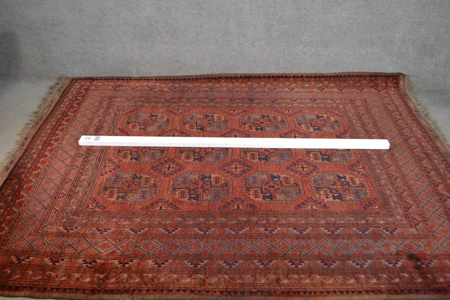 A handmade Afghan carpet with repeating gul motifs on a burgundy field within stylised borders. L. - Image 2 of 7