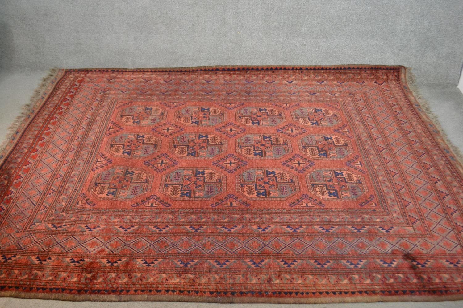A handmade Afghan carpet with repeating gul motifs on a burgundy field within stylised borders. L.