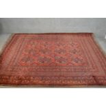 A handmade Afghan carpet with repeating gul motifs on a burgundy field within stylised borders. L.