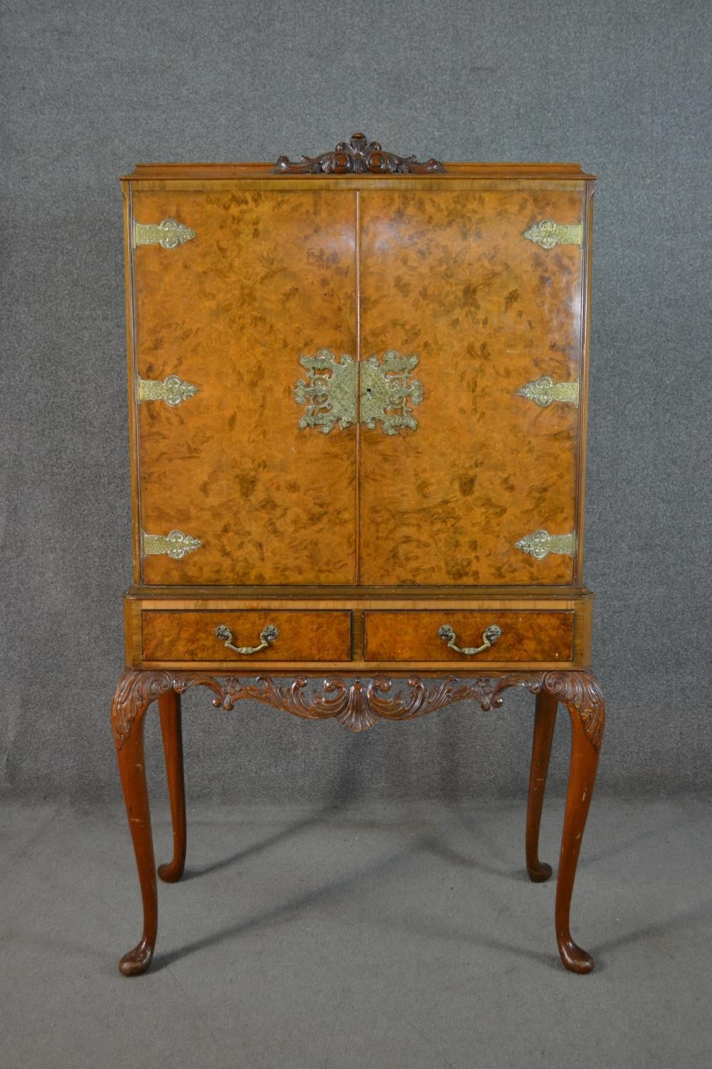 An Epstein style 1930s burr walnut drinks cabinet, the two cupboard doors with ornate brass