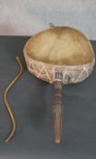 An African hide and gut drum with carved handle and beating stick. L.67 W.37cm