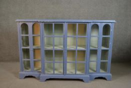 A grey painted wood breakfront display cabinet, with four glazed doors enclosing shelves, on bracket