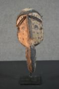 An early 20th century carved and painted African Tribal mask on metal display stand. H.37cm (inc.