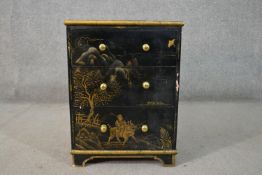 A circa 1920s Chinese style black lacquered bedside chest, painted and gilded with landscapes and