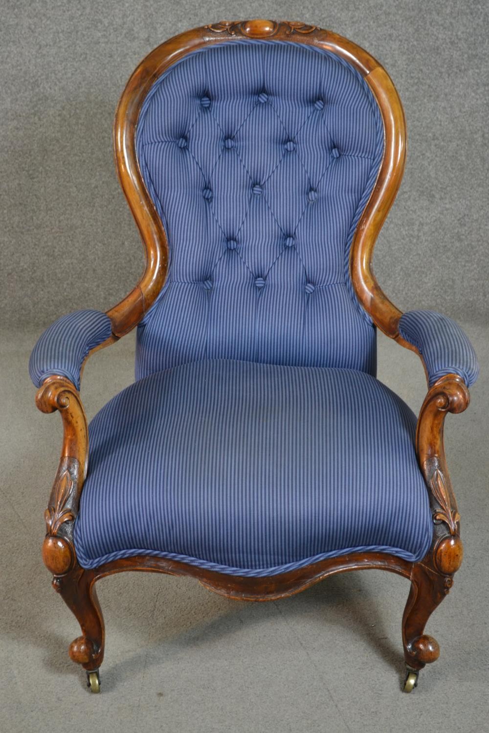 A Victorian walnut spoon back open armchair, upholstered in striped blue fabric, to the arms, seat