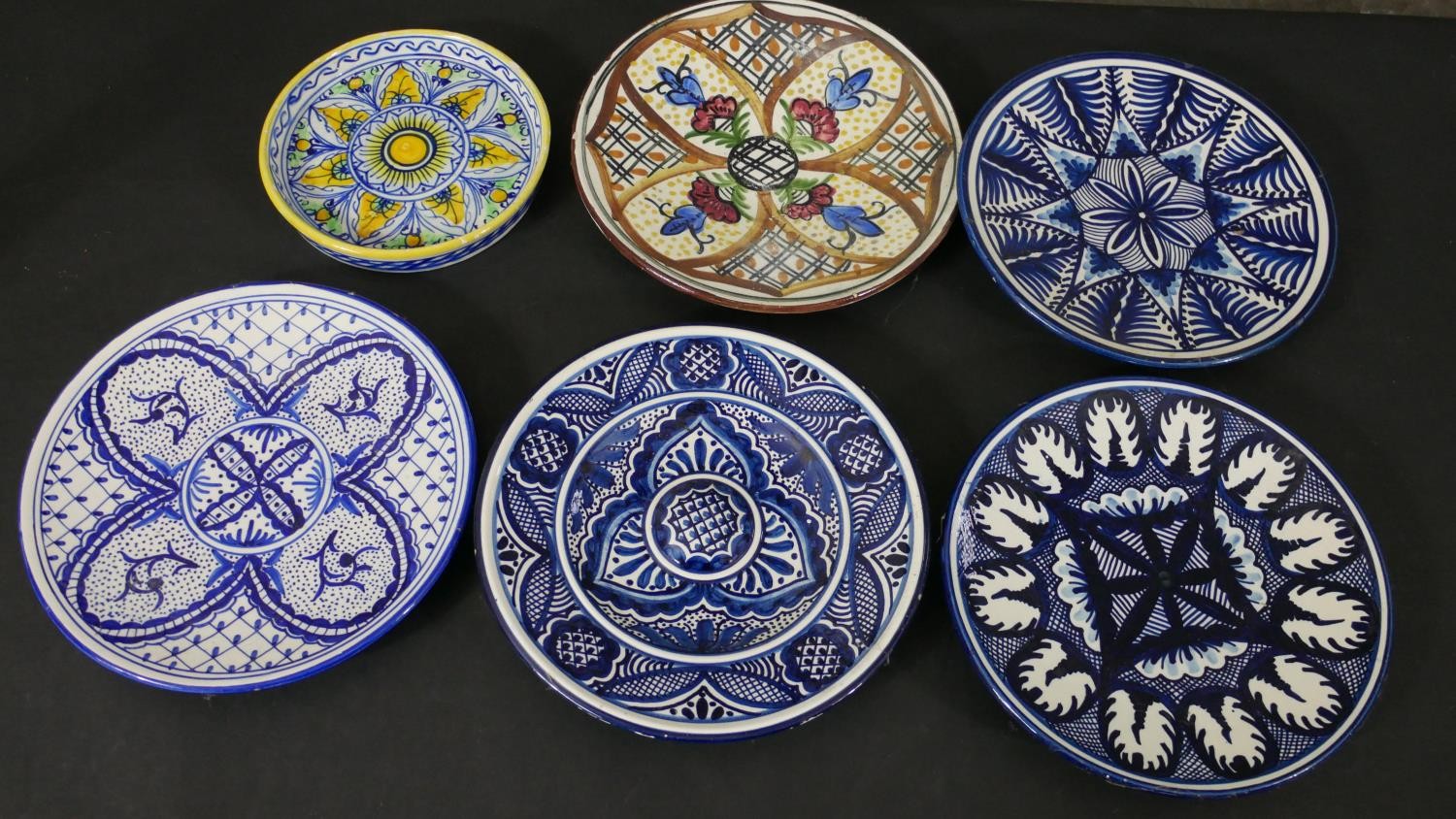 A collection of six majolica ceramic hand painted chargers, each with a different design, some