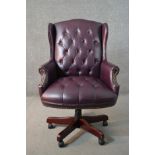 A 20th century wing back swivel office chair, upholstered in burgundy leather, with buttoned back