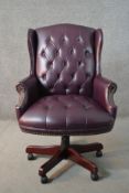 A 20th century wing back swivel office chair, upholstered in burgundy leather, with buttoned back