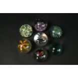 A collection of seven art glass paperweights, including a Caithness black 'Flower in the Rain'