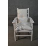 An early 20th century white painted oak reclining armchair, with loose cushions, the adjustable back