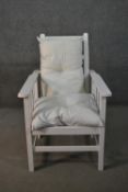 An early 20th century white painted oak reclining armchair, with loose cushions, the adjustable back
