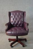 A 20th century wing back swivel office chair, upholstered in burgundy leather, with buttoned back