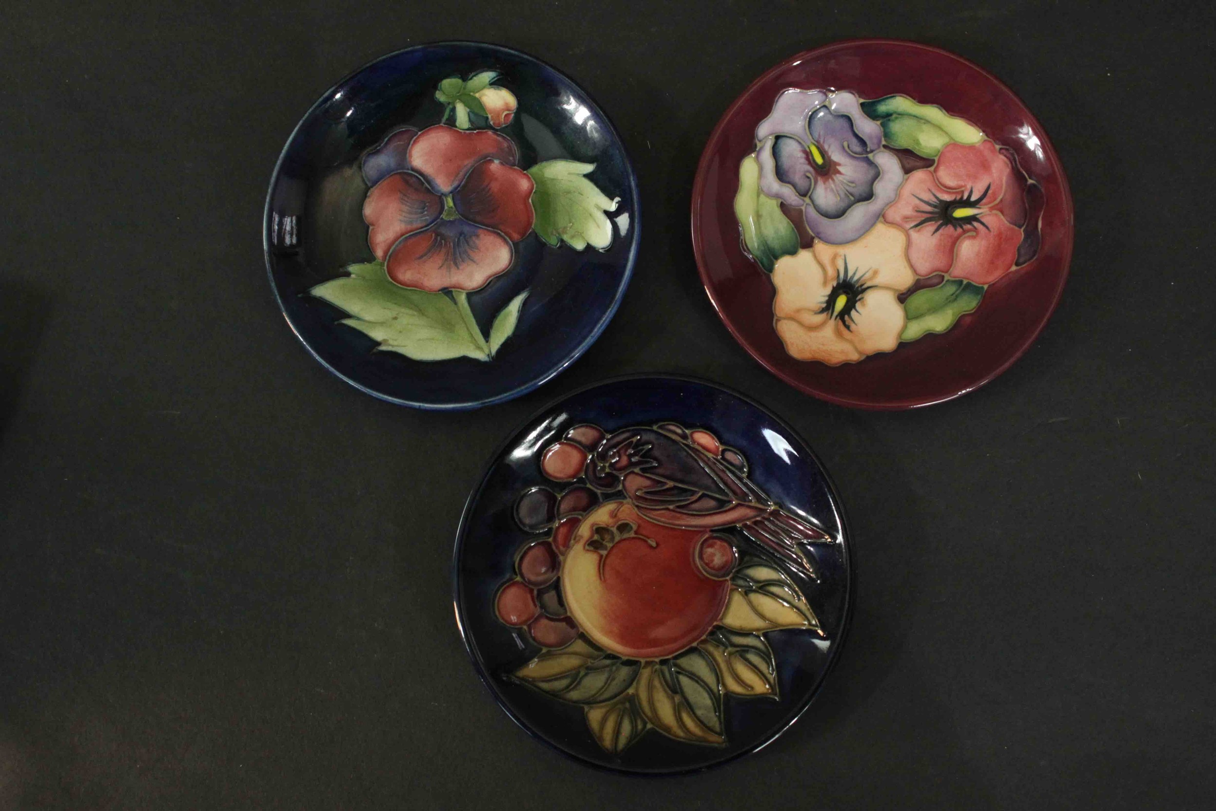 Three Moorcroft pottery dishes. Pansy and bird and fruit pattern, makers mark to the base. Dia.12cm.