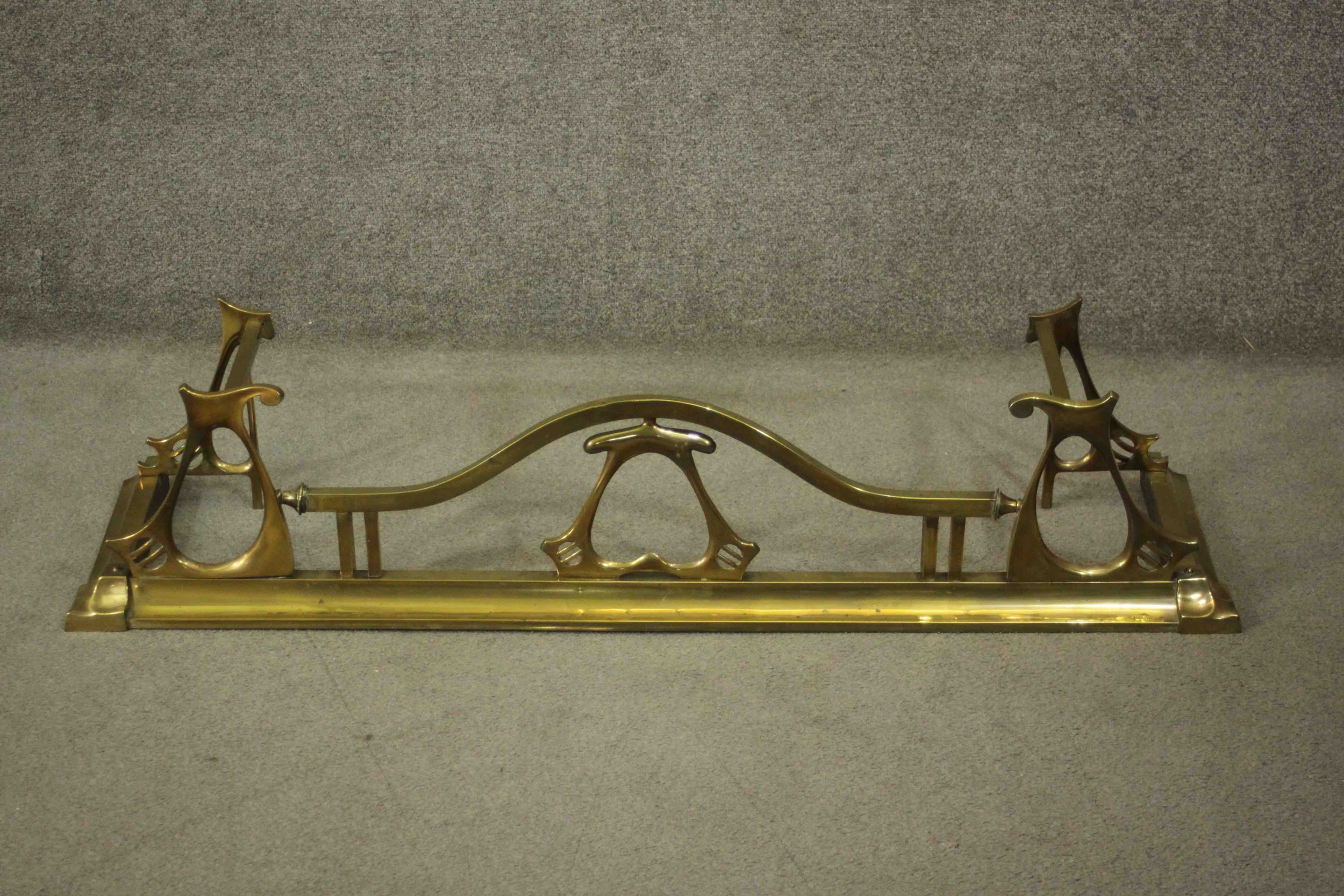 A 19th Century Art Nouveau brass fire fender with sloped edge with typical Art Nouveau scroll work