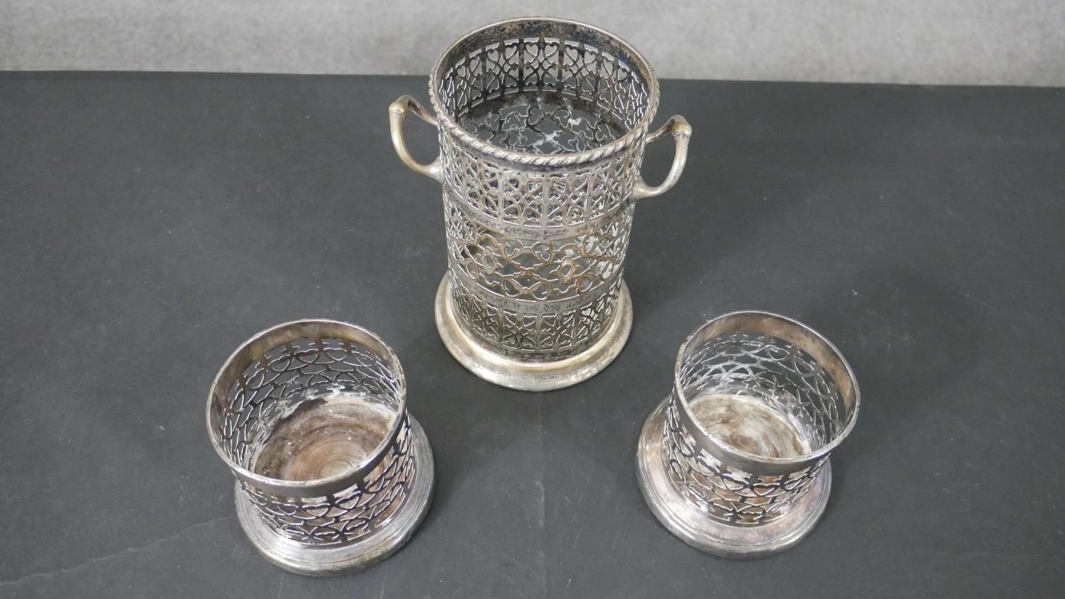 A pair of silver plated pierced design wine coasters and a similar twin handled bottle holder. H.