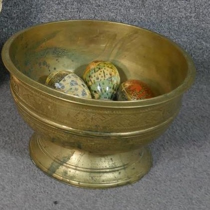 An Indian brass pedestal bowl filled with eight hand painted papier mache eggs.