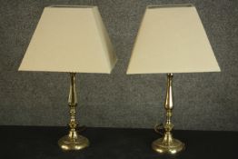 A pair of brass table lamps, with baluster stems and circular bases, with ivory coloured shades. H.